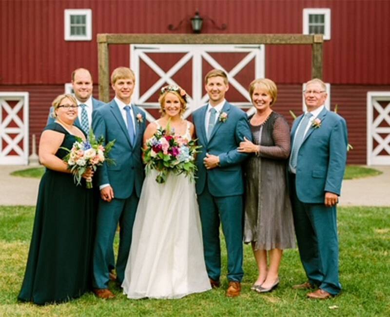 Photo of family standing outside of a red barn on a wedding day